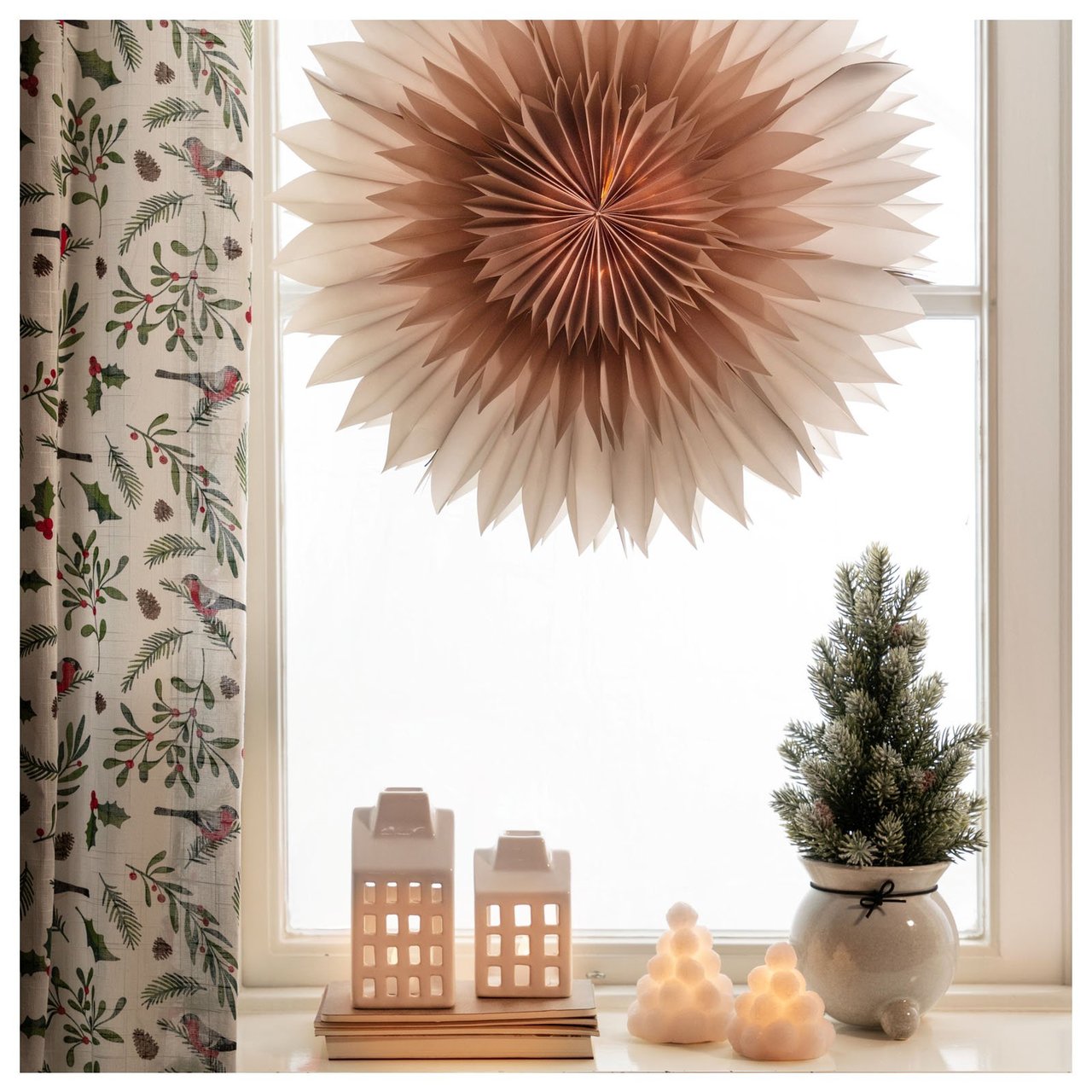 Ein kleiner Kunstbaum im beigen Topf im Fenster.