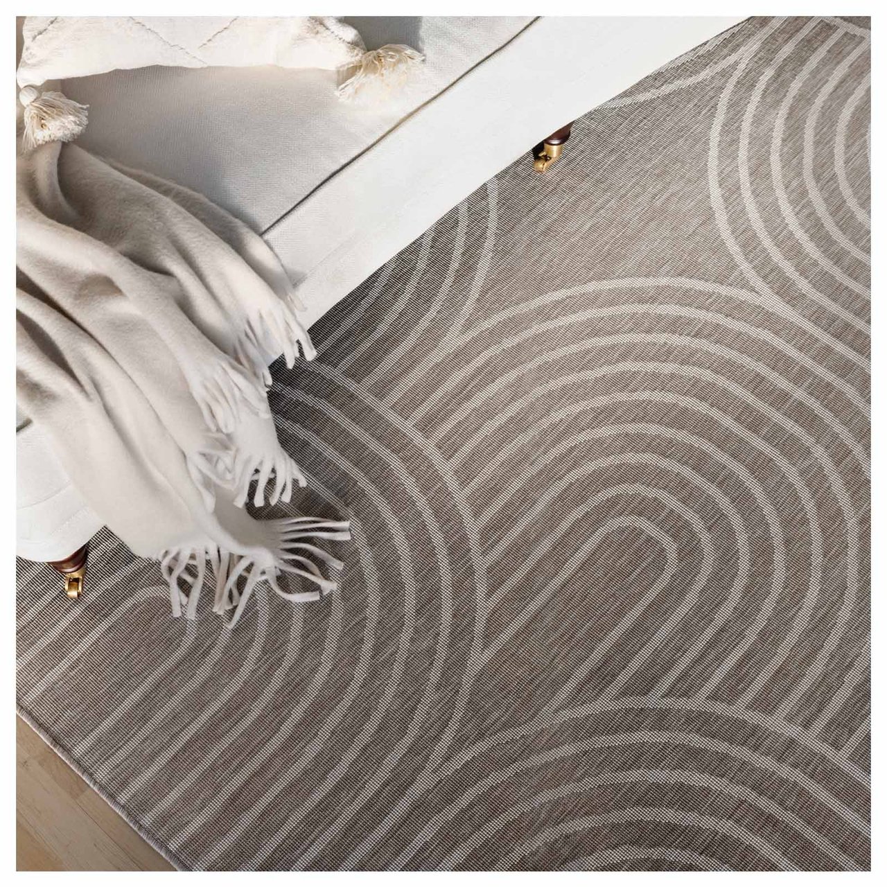 Sohvannurkka, jossa on koristeellinen torkkupeitto ja tyyny sekä beigen värinen kuviollinen matto.