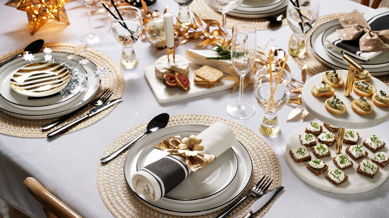 Elegante Neujahrstafel in Weiß und Gold mit Geschirr, Servietten und festlicher Deko.