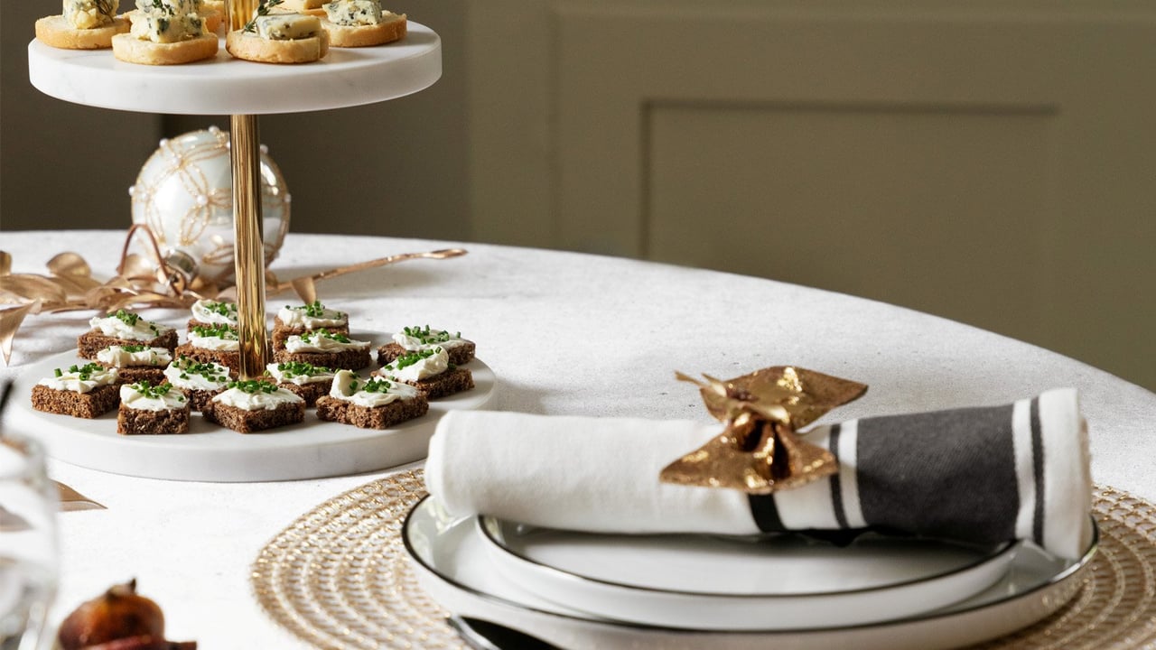 Elegant nyårsdukning i vitt och guld med porslin, servetter och festliga dekorationer på ett dukat bord.