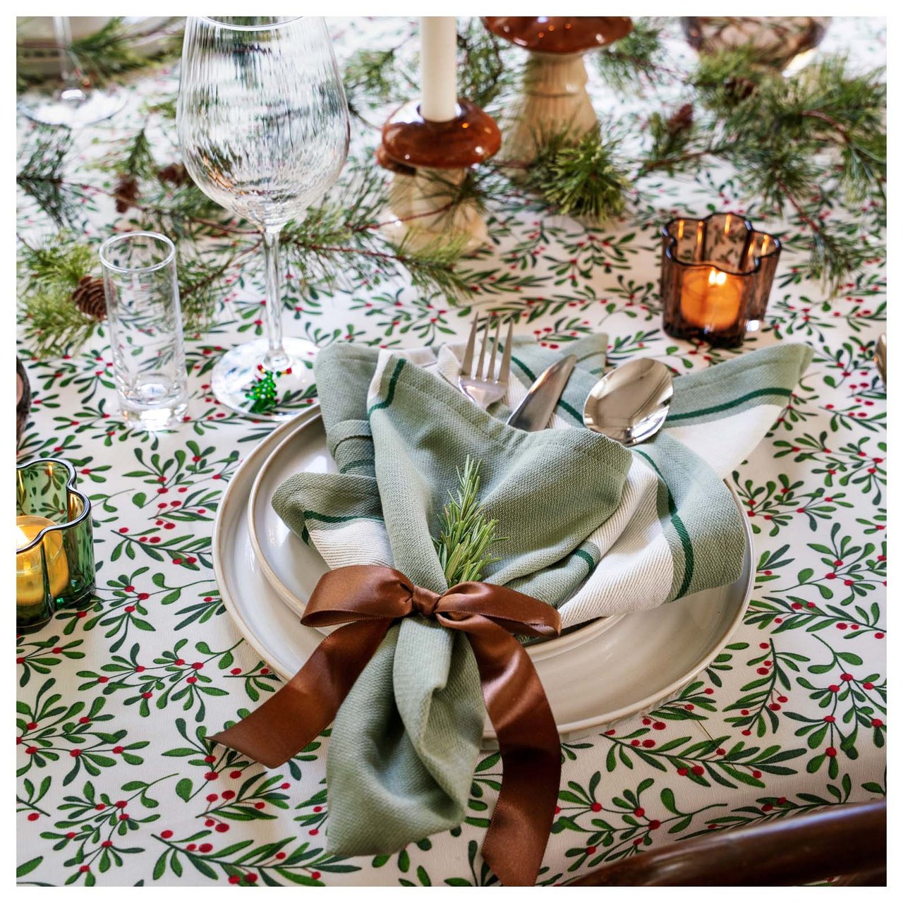 Joulukattaus skandinaaviseen tyyliin lautasella, lasilla ja nauhalla sekä vihreällä oksalla koristellulla lautasliinalla.