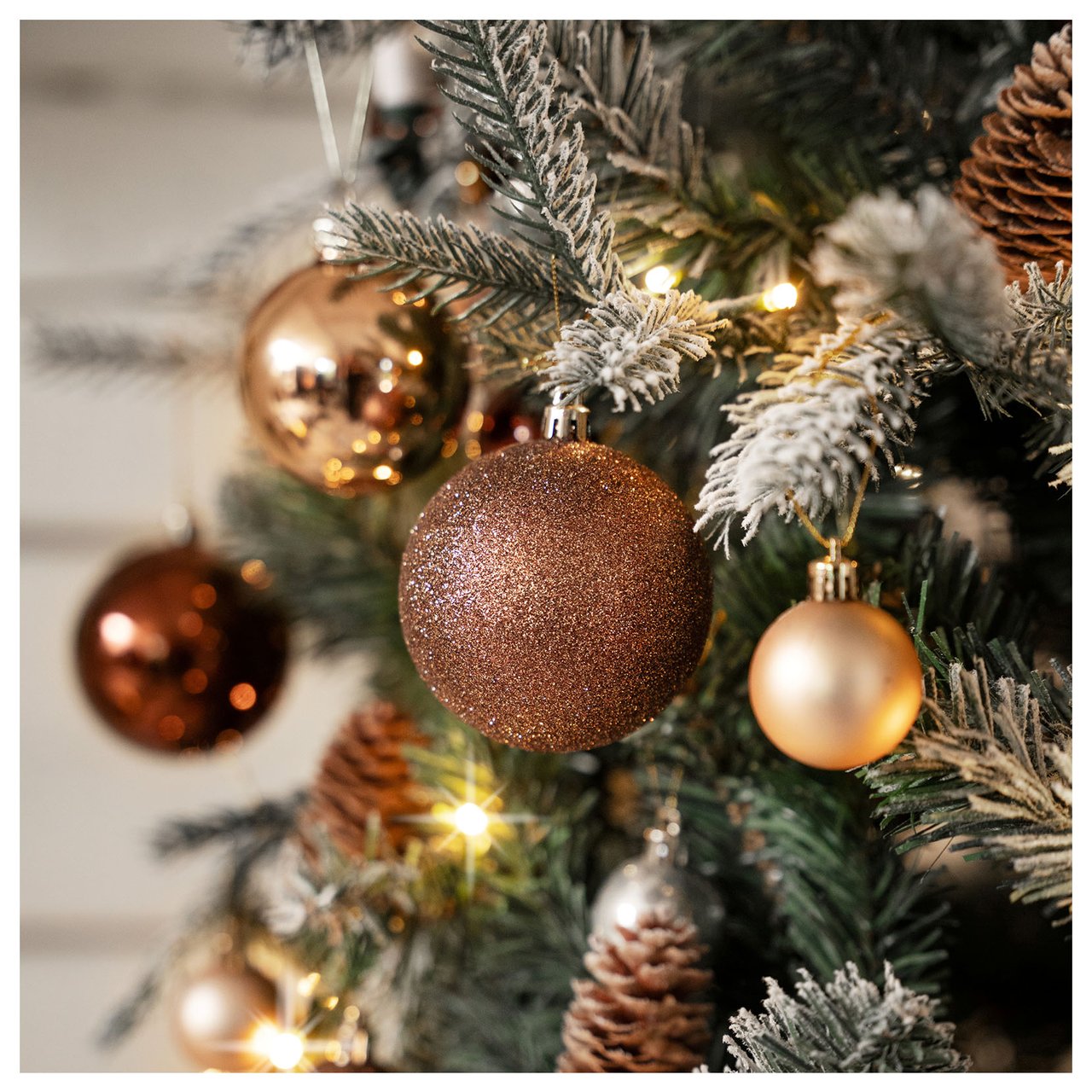 Nahaufnahme eines mit Tannenzapfen und glänzenden Kugeln geschmückten Weihnachtsbaums in warmen Farbtönen.