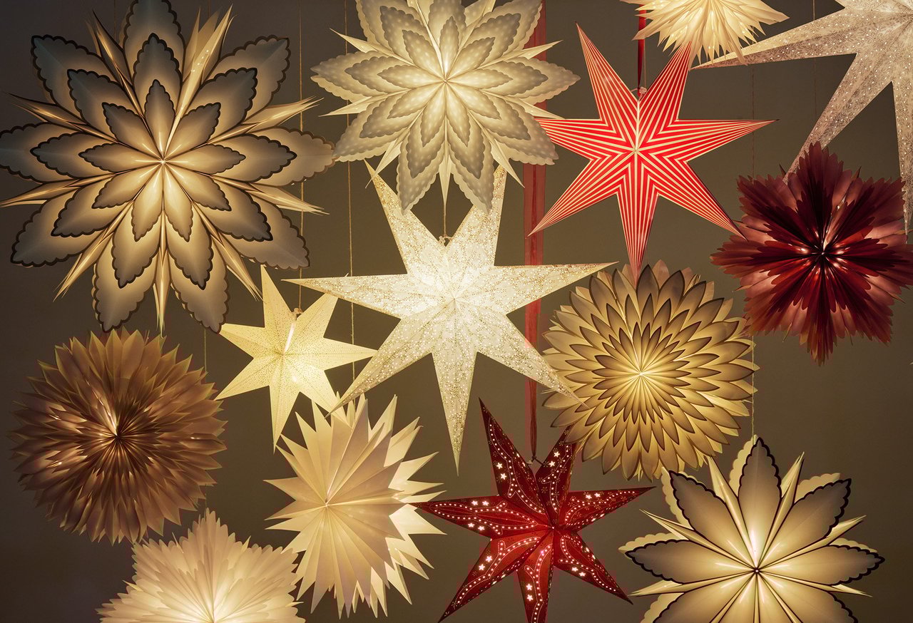 Mehrere dekorative Adventssterne in verschiedenen Formen leuchten in einer Gruppe vor dunklem Hintergrund.