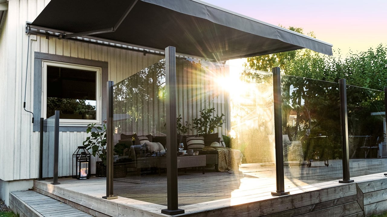 Stor altan med glasräcken och terrasmarkis i solnedgång.