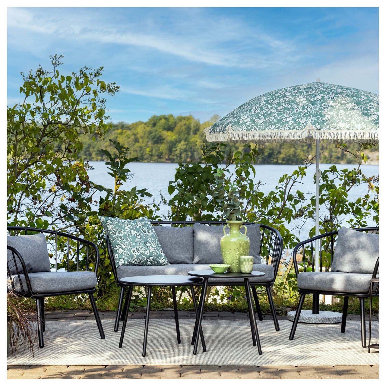 Gemütliche Terrasse mit einer Lounge-Gruppe mit grauen Polsterauflagen und einem gemusterten Kissen, das zum Sonnenschirm passt.