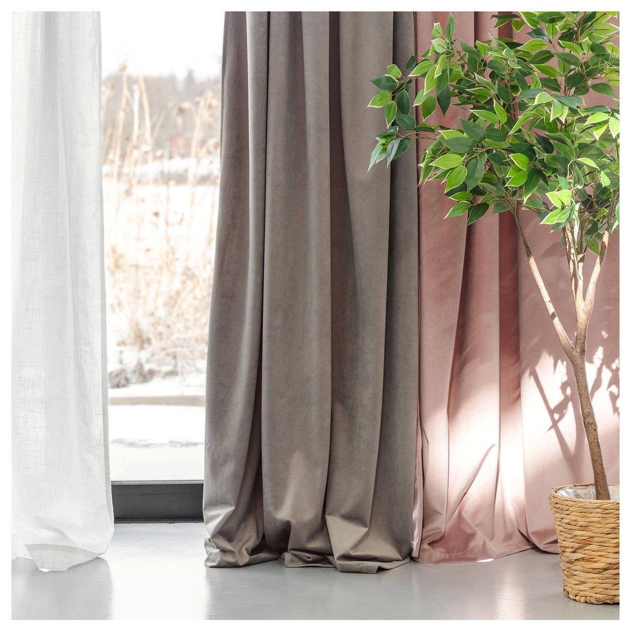 Fönster med flera lager med gardiner i ljusa färger och en grön växt i kruka placerad intill.