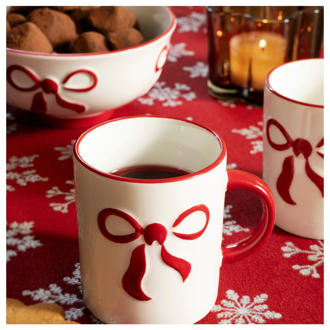 Weiße Glöggbecher und Schale mit roten Schleifen auf roter Tischdecke.