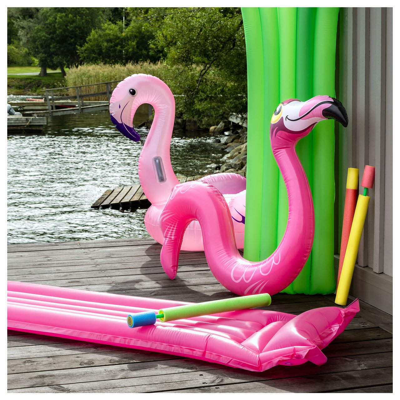 Farbenfrohes Badespielzeug, ein aufblasbarer Flamingo, eine rosa Luftmatratze und Wasserspielzeug aus Schaumstoff, bereit für den Sommer am Badesteg.