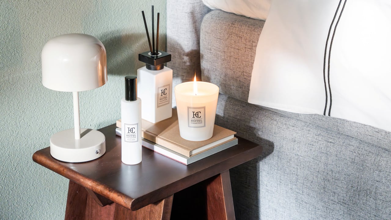 Alt-texter sade:  Ett nattduksbord intill en säng är stylat med lampa, doftprodukter och böcker för en hotellinspirerad känsla.