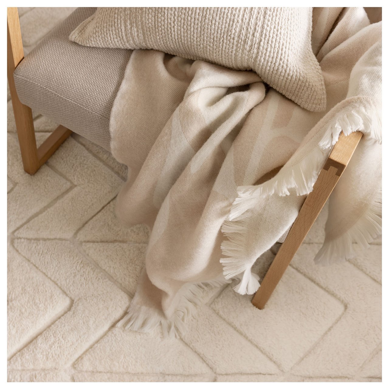 Beigefarbene Decke und Kissen auf einem Stuhl.