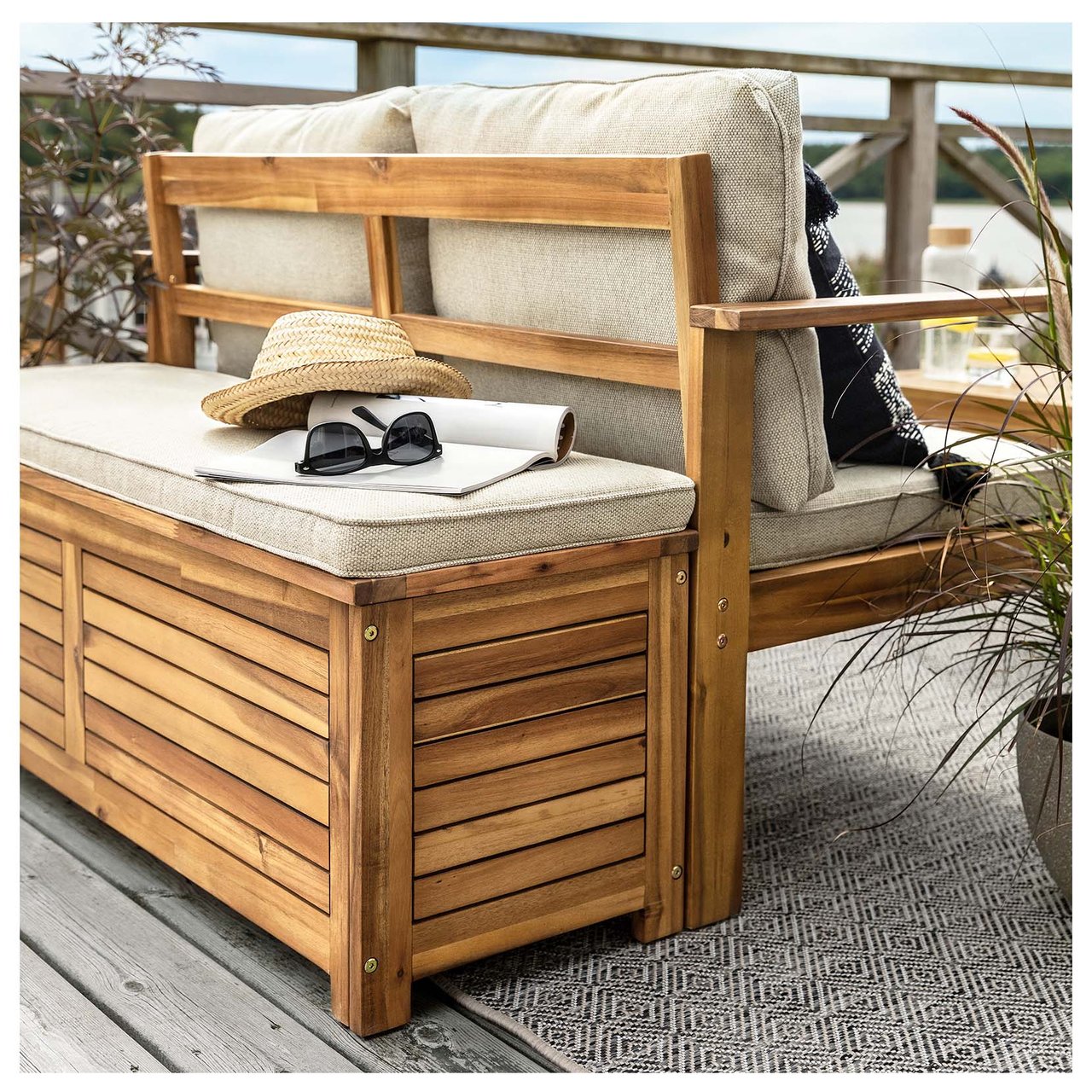 Dynbox i trä med sittdyna står mot ryggen på en utomhussoffa. På boxen ligger solhatt och solglasögon.