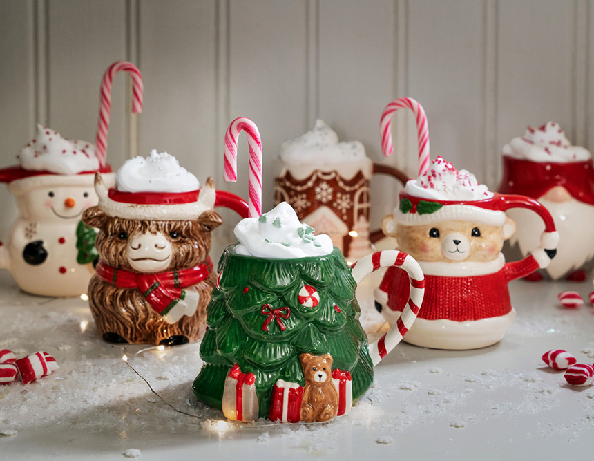 Verspielte Weihnachtsbecher mit Sahne und Zuckerstangen stehen auf einem Tisch mit Winterdekoration.