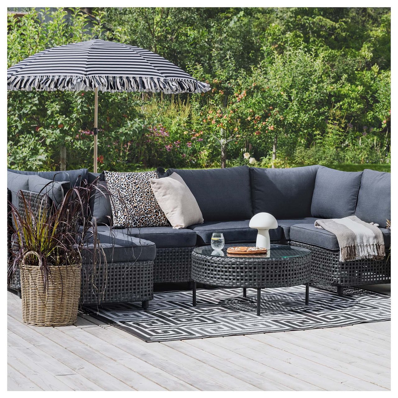 Großes Ecksofa mit beigen Sitzkissen auf einer Terrasse vor einer Hauswand. Das Sofa hat beige Sitzkissen, ein Couchtisch ist mit einer Solarlampe dekoriert.