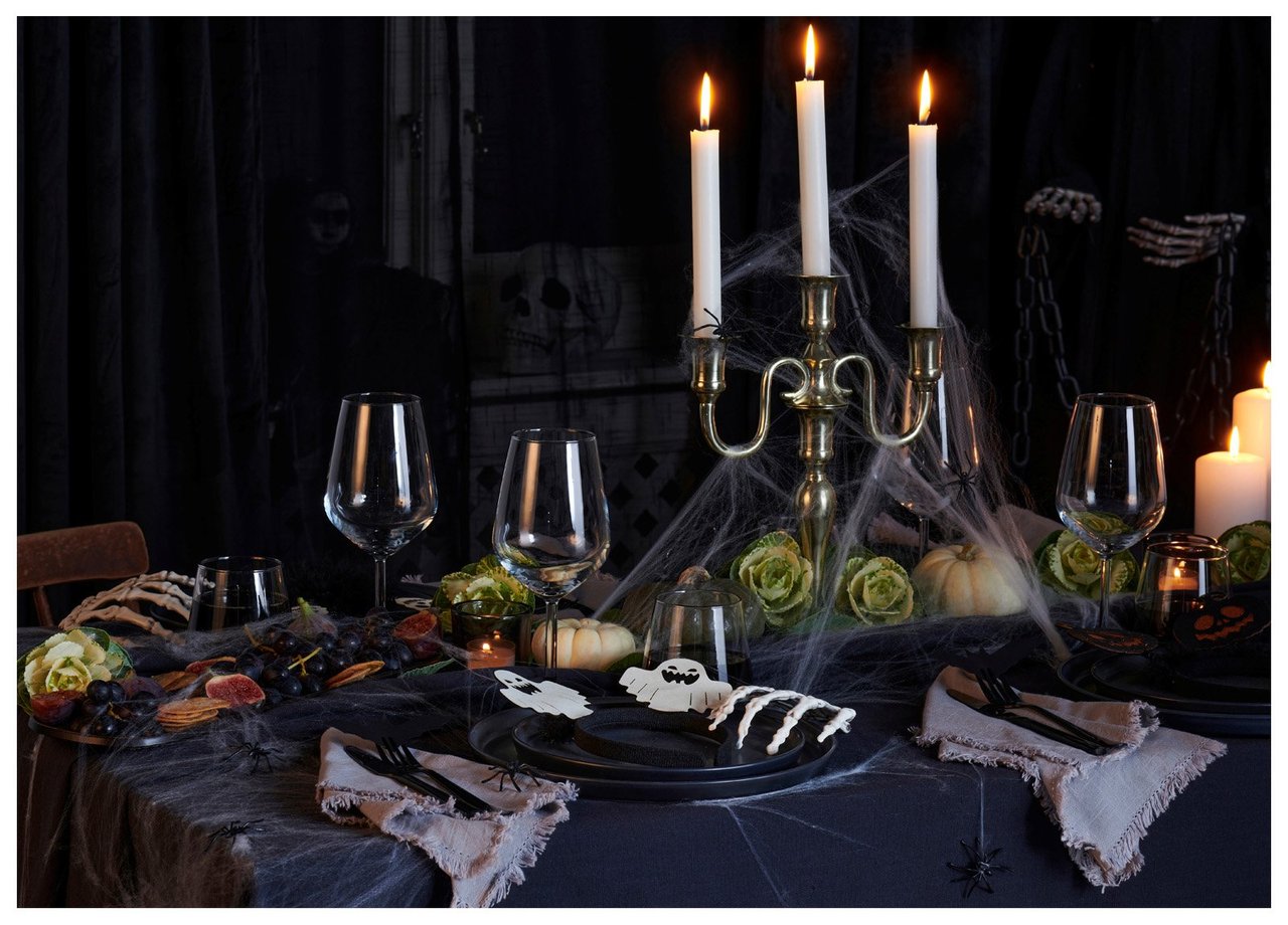 Halloween-inspirert dekorasjon med kandelabre, spindelvev, pynt og tente lys i mørkt miljø.