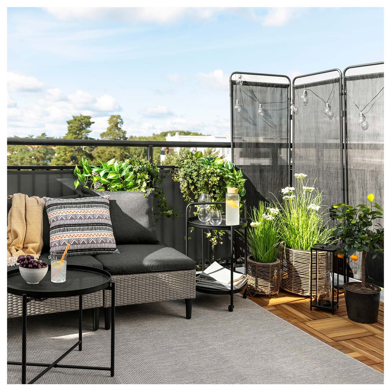 Stor solrik balkong med innsynsskjerming, masse grønne vekster og loungedel med sofa og bord.