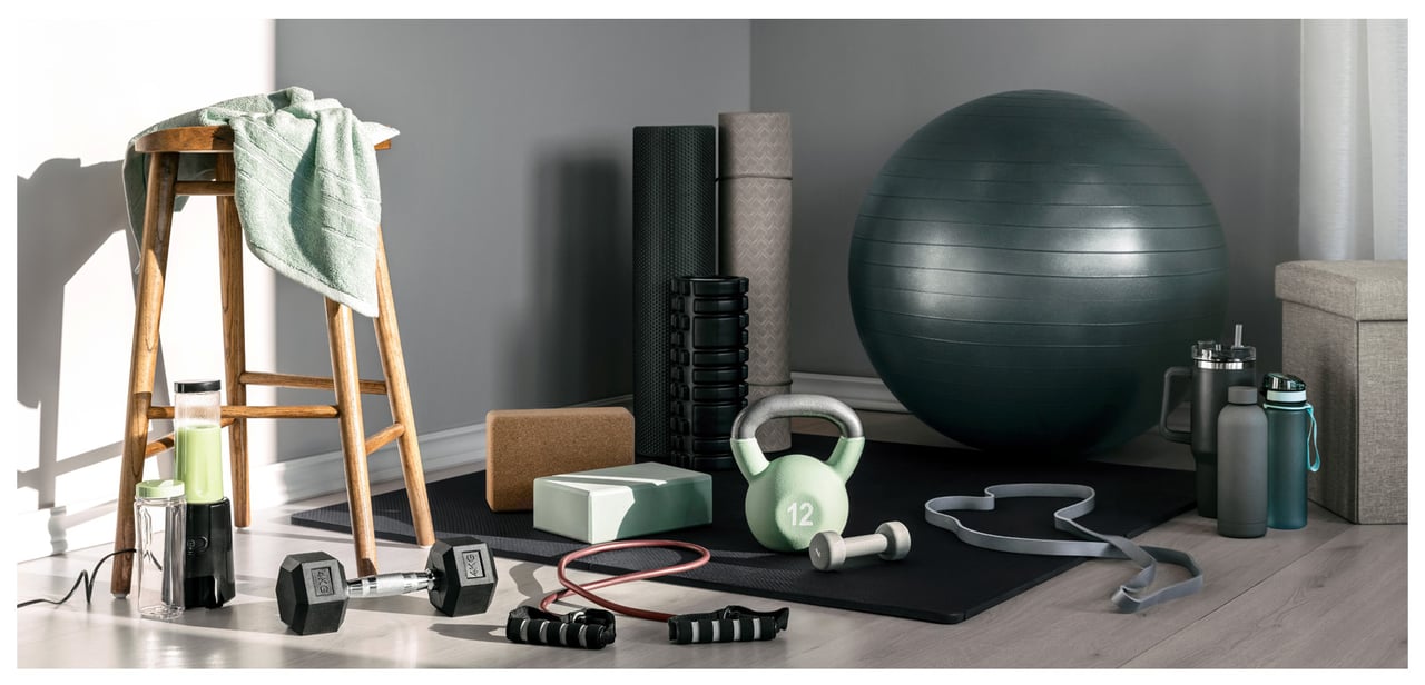 Hemmagym med träningsmattor, balansboll, vikter, redskap, vattenflaskor och handduk i solljus.