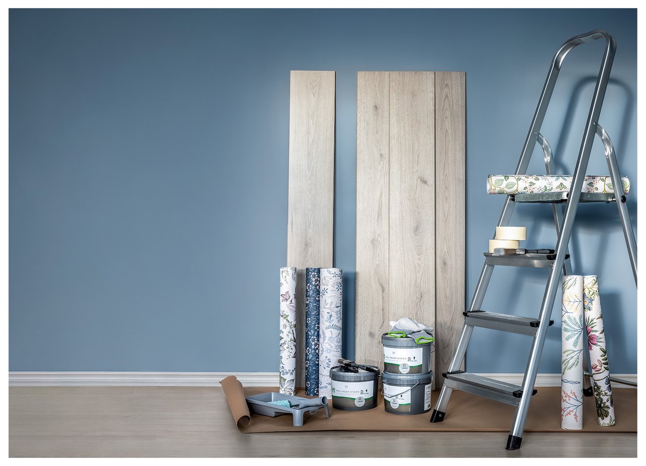 Maalausprojekti, jossa näkyvät tikkaat, tapettirullilla, maalipurkkeja ja lattialankkuja sinistä seinää vasten.