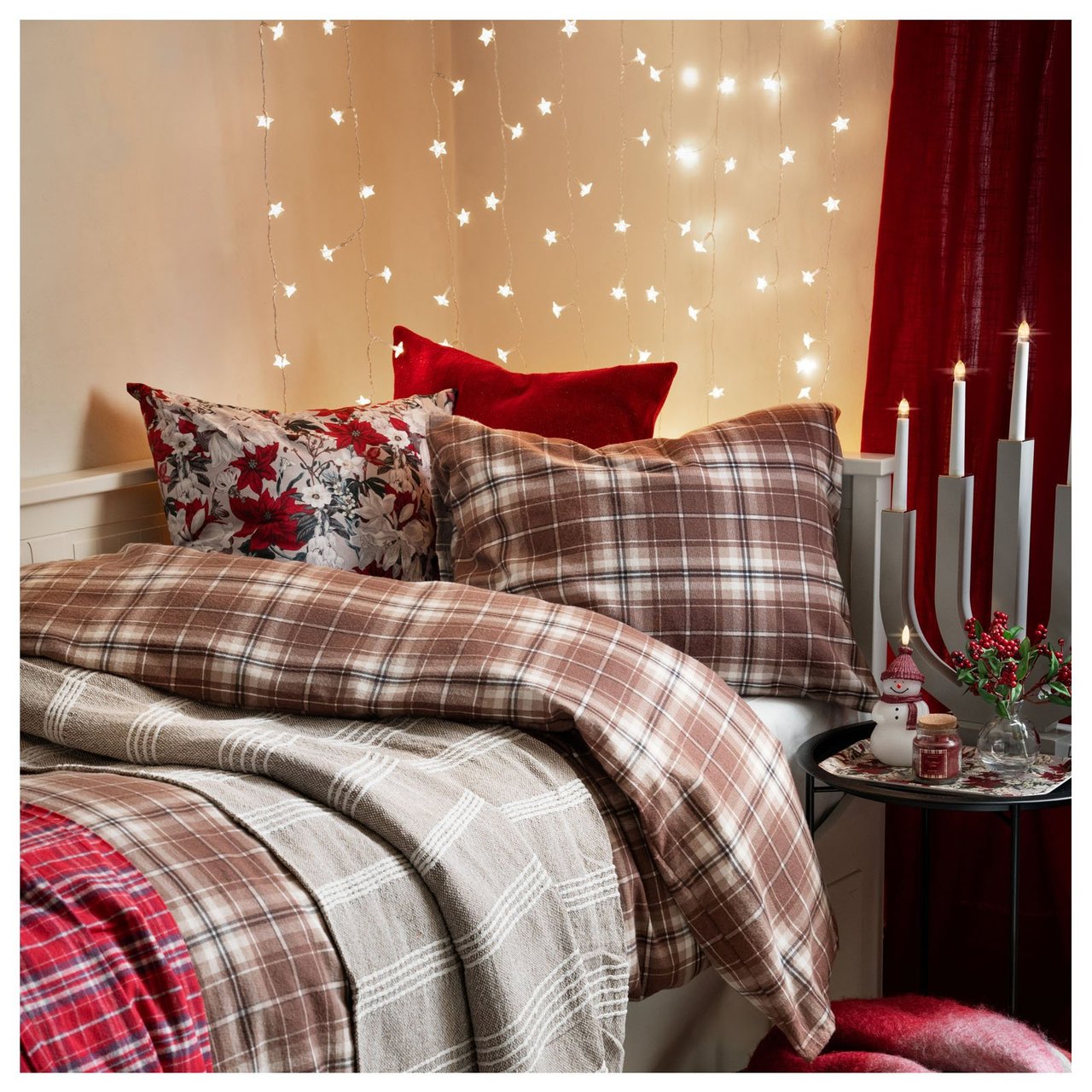 Ein Bett, bezogen mit weihnachtlichen Textilien. Ein Lichtervorhang hängt hinter dem Kopfende, als alternative Bettkopflehne.