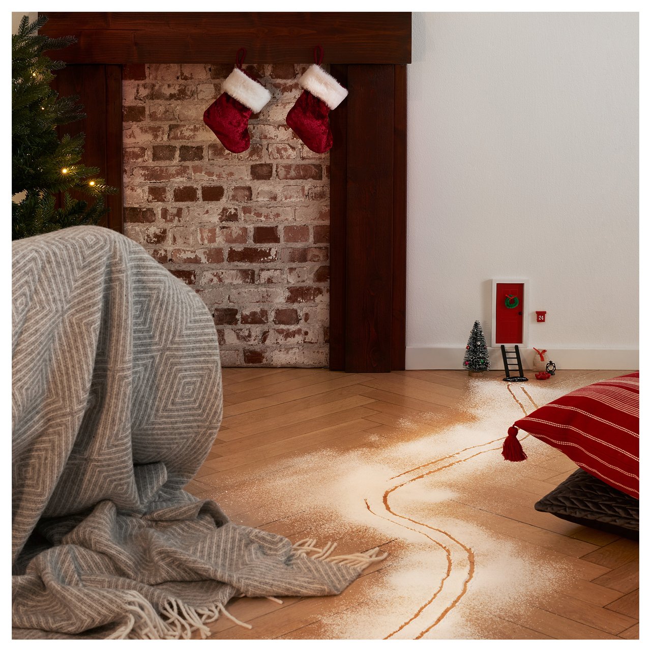 Skispuren aus Mehl führen über den Boden zu einer Wichteltür am weihnachtlichen Kamin.