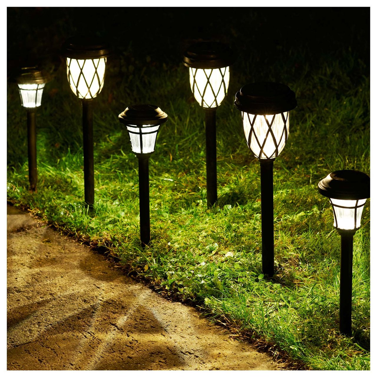 Solcellsbelysning i form av spjut är nerstuckna på rad i gräset intill en grusgång.