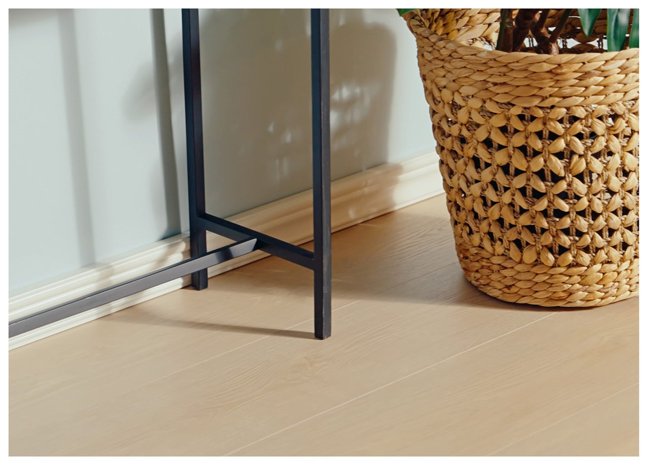 Närbild på ett laminatgolv i hemmiljö med en växt i korg och ett sidobord som inredningsdetaljer.