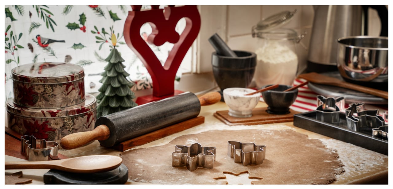 En utkjevlet pepperkakedeig med kjevle og pepperkakeformer. En adventsstake i bakgrunnen.