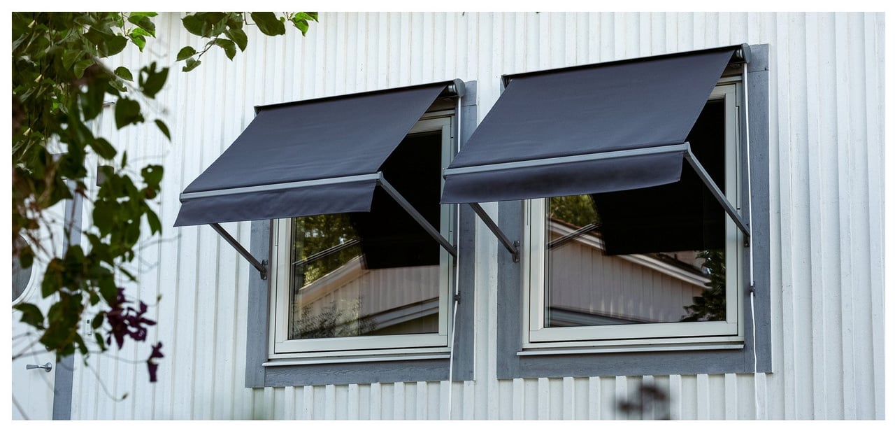Suuri harmaa markiisi oleskelualueen yllä pihalla. Kaksi pientä punaraitaista markiisia avattuna kahden ikkunan yläpuolella.