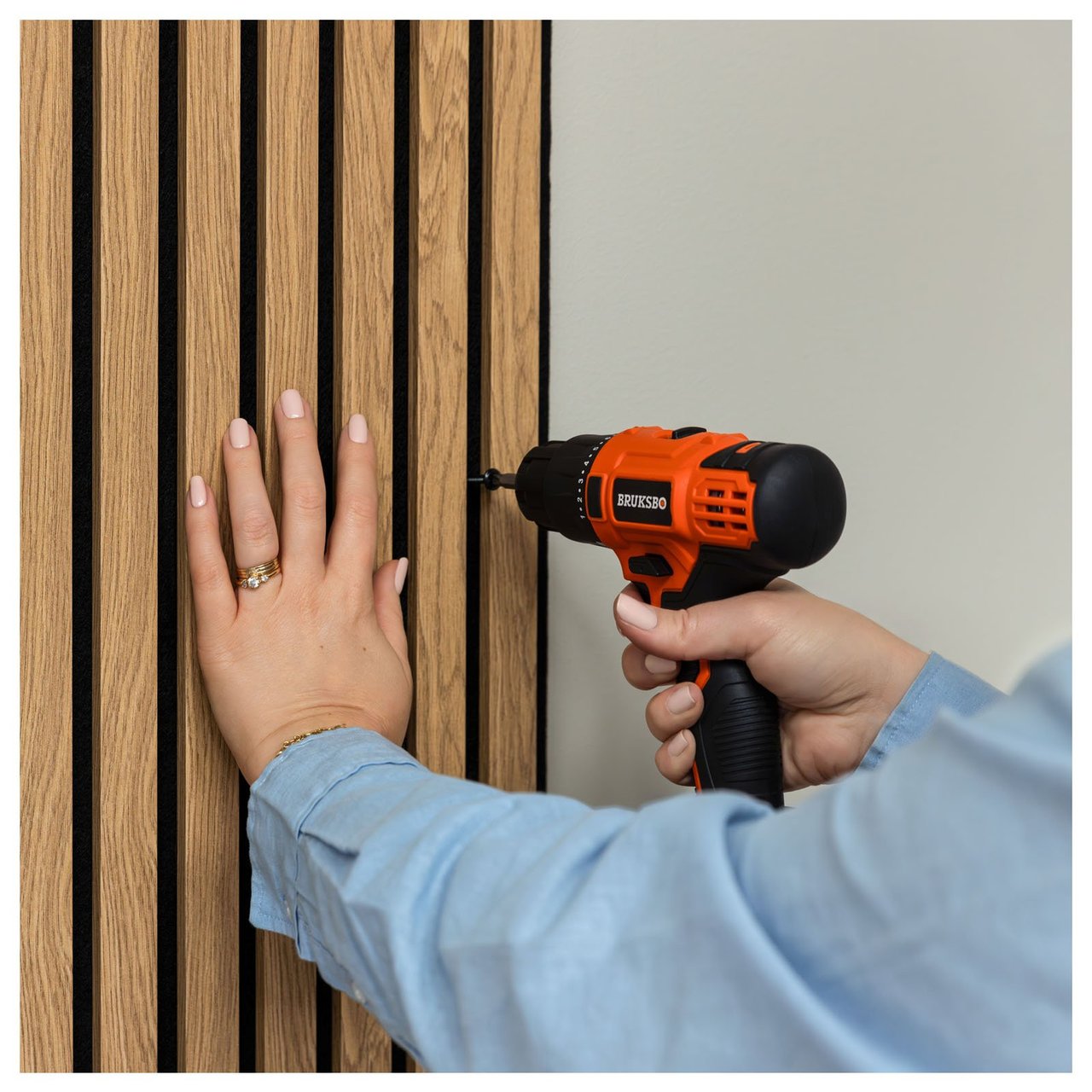 En person monterar akustikpanel på vägg med hjälp av en skruvdragare.