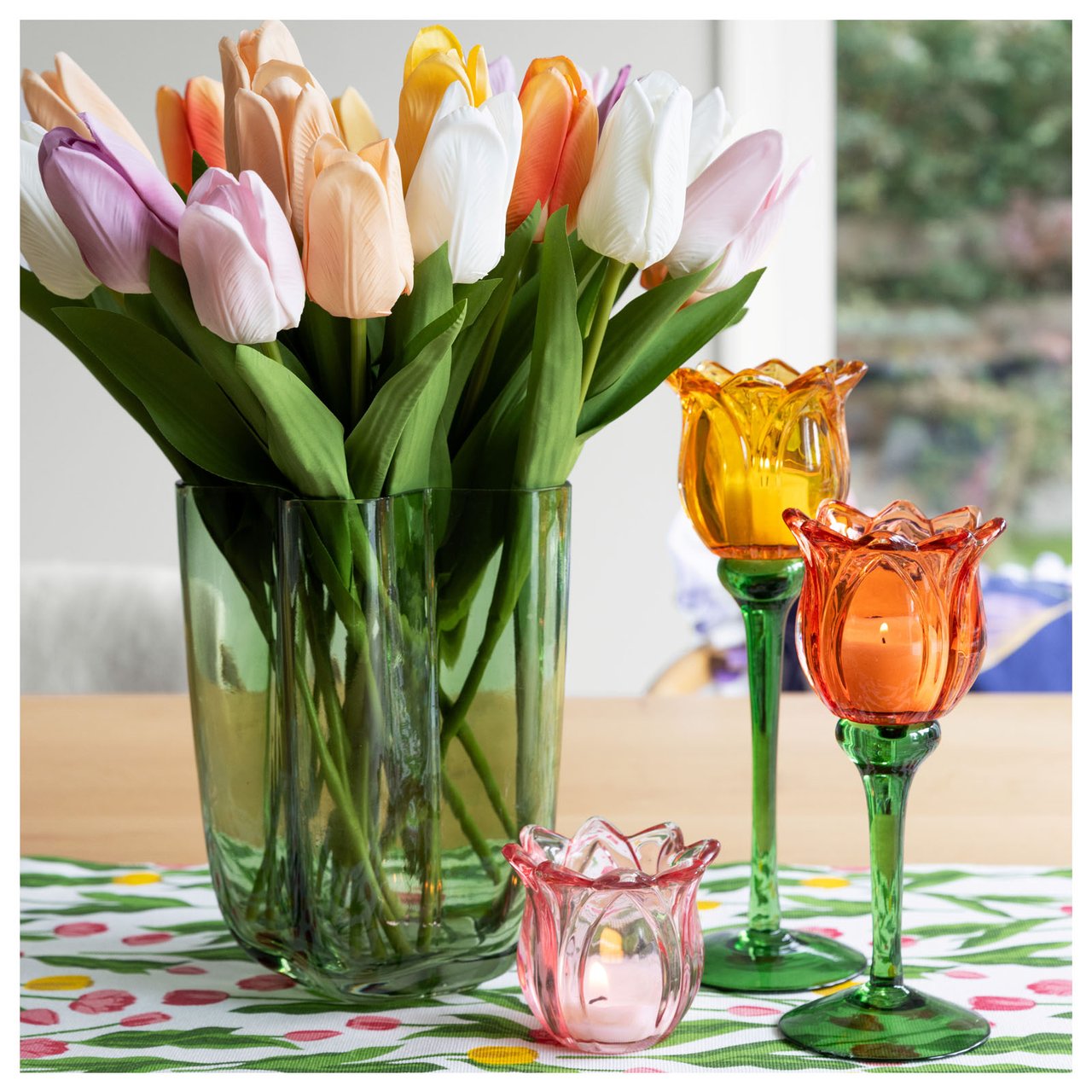 Tulppaanimaljakko ja kukkakuvioiset kynttilänjalat katetulla pöydällä.