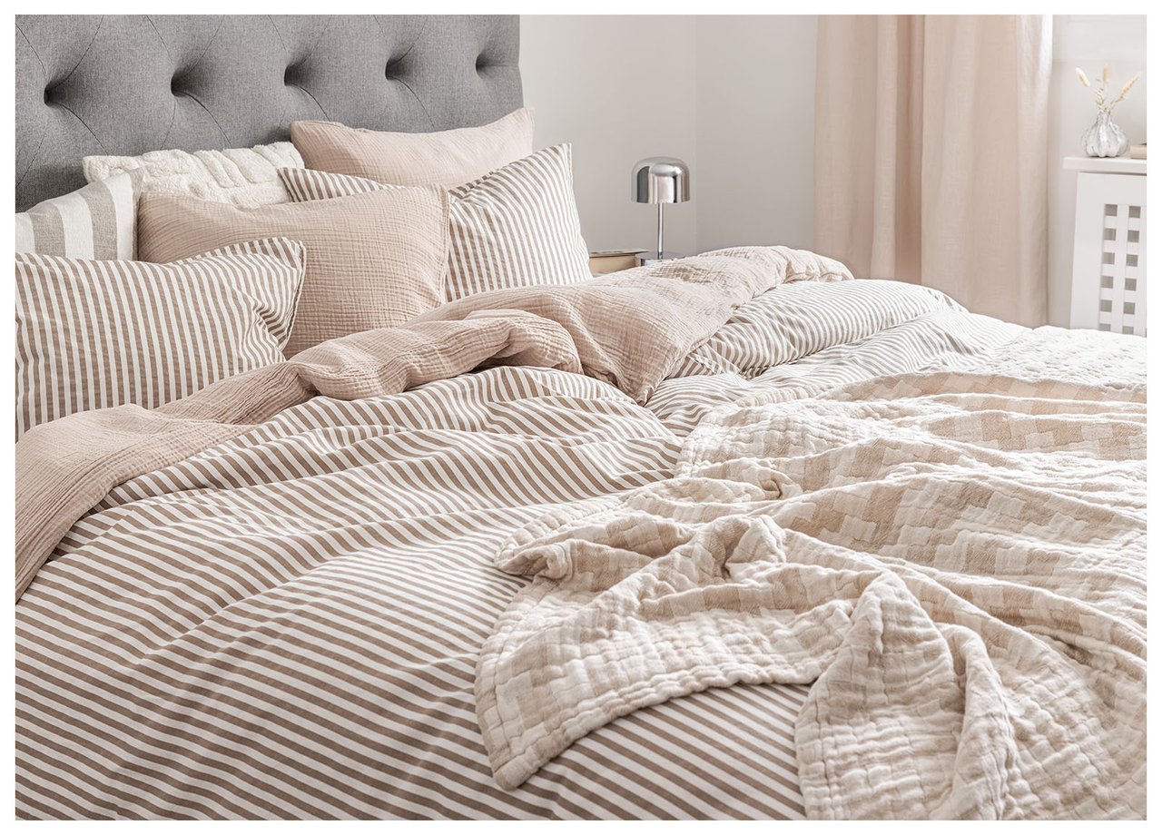 Doppelbett mit mehreren Kissen, bezogen in einer beigen Farbskala. Eine Tagesdecke ist lässig über das Bett geworfen.