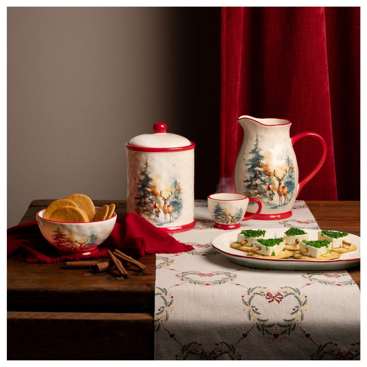 Kupit ja tarjoiluastiat, joilla on keksejä ja voileipiä jouluiseksi katetulla pöydällä.