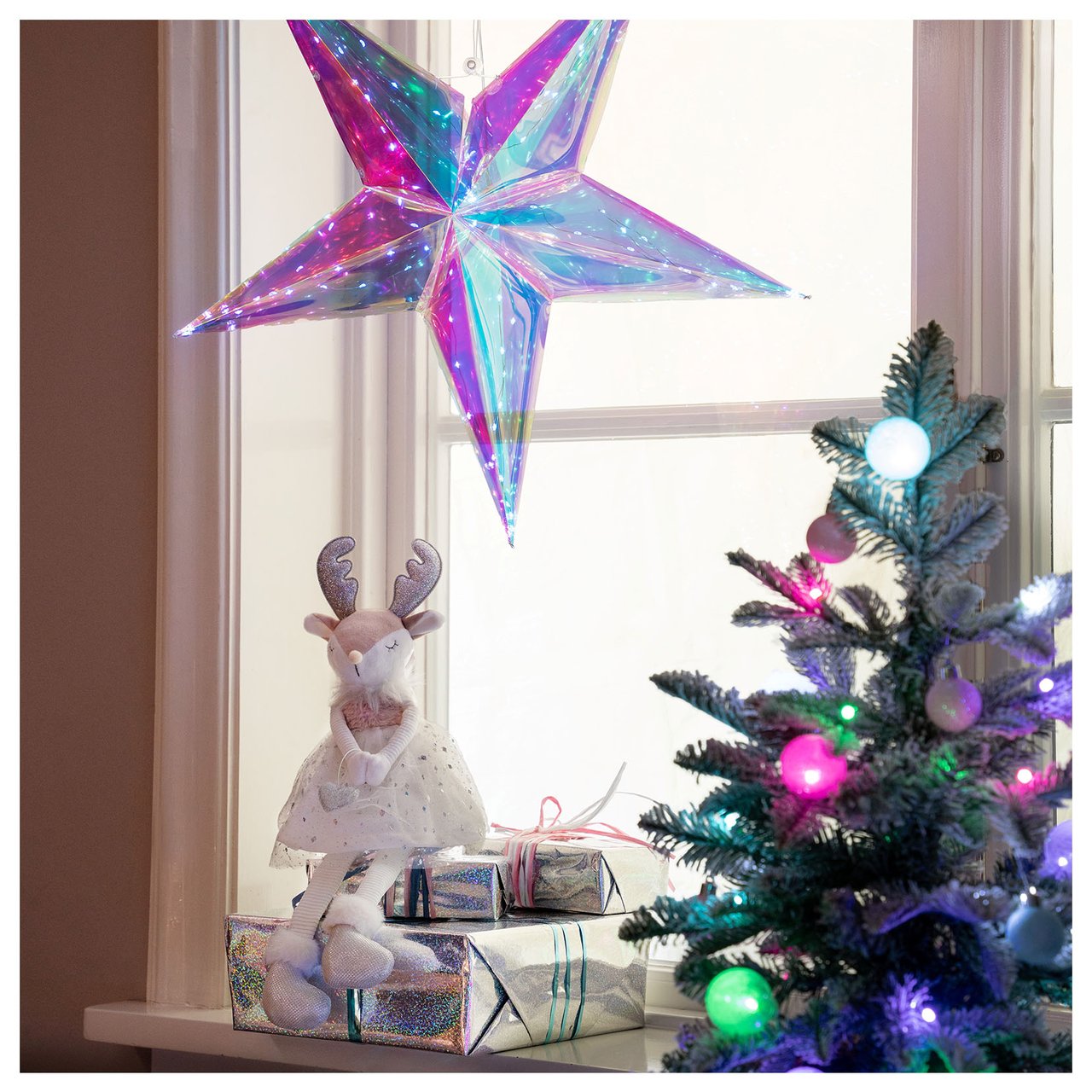 Glitzernder Stern im Fenster mit Deko-Rentier, Mini-Weihnachtsbaum und Geschenken darunter.