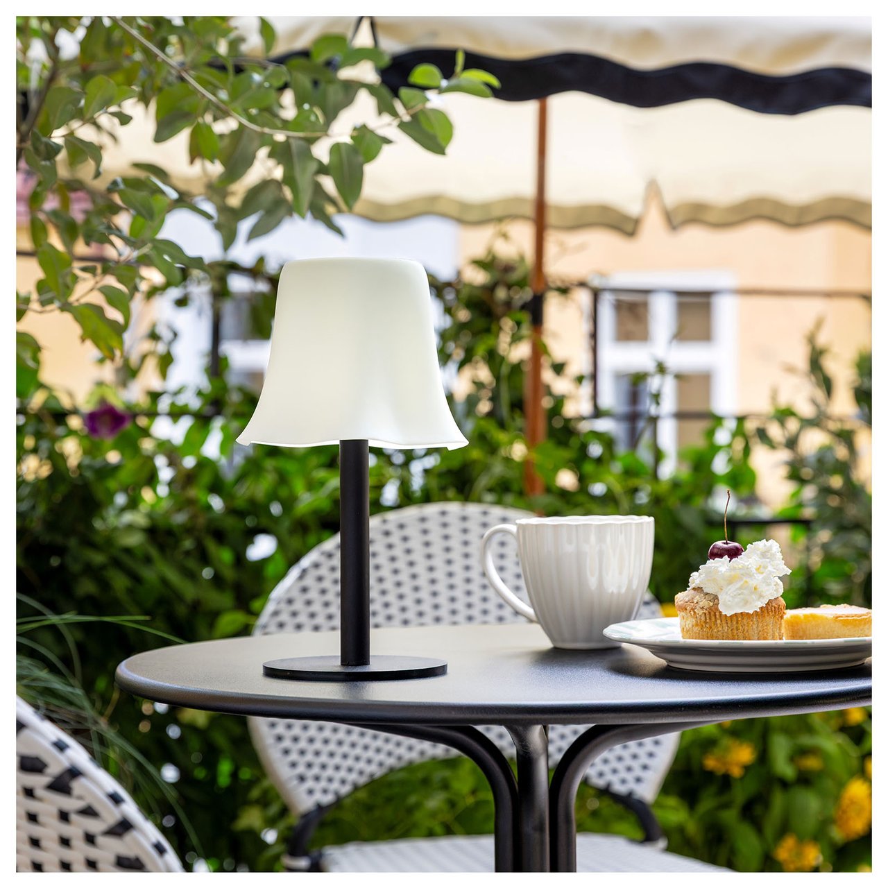 En liten lampe med svart fot og hvit lampeskjerm med bølgete kant på et bord.
