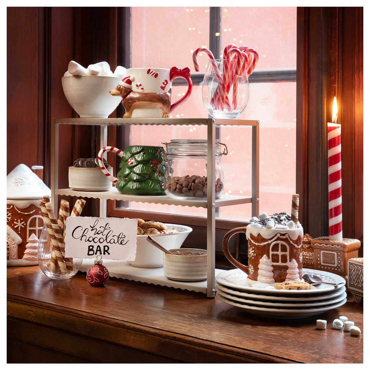 En hot chocolate bar med julmuggar, polkagrisar och marshmallows står uppdukad i ett fönster. 
