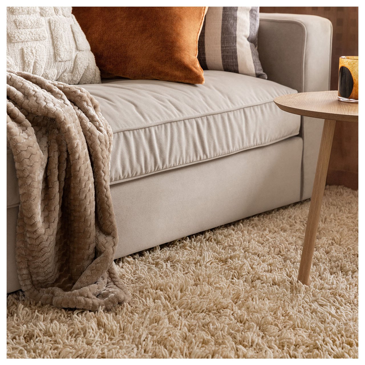 Wohnzimmer mit Sofa, Zierkissen, beiger Wollteppich und kleinem Couchtisch.