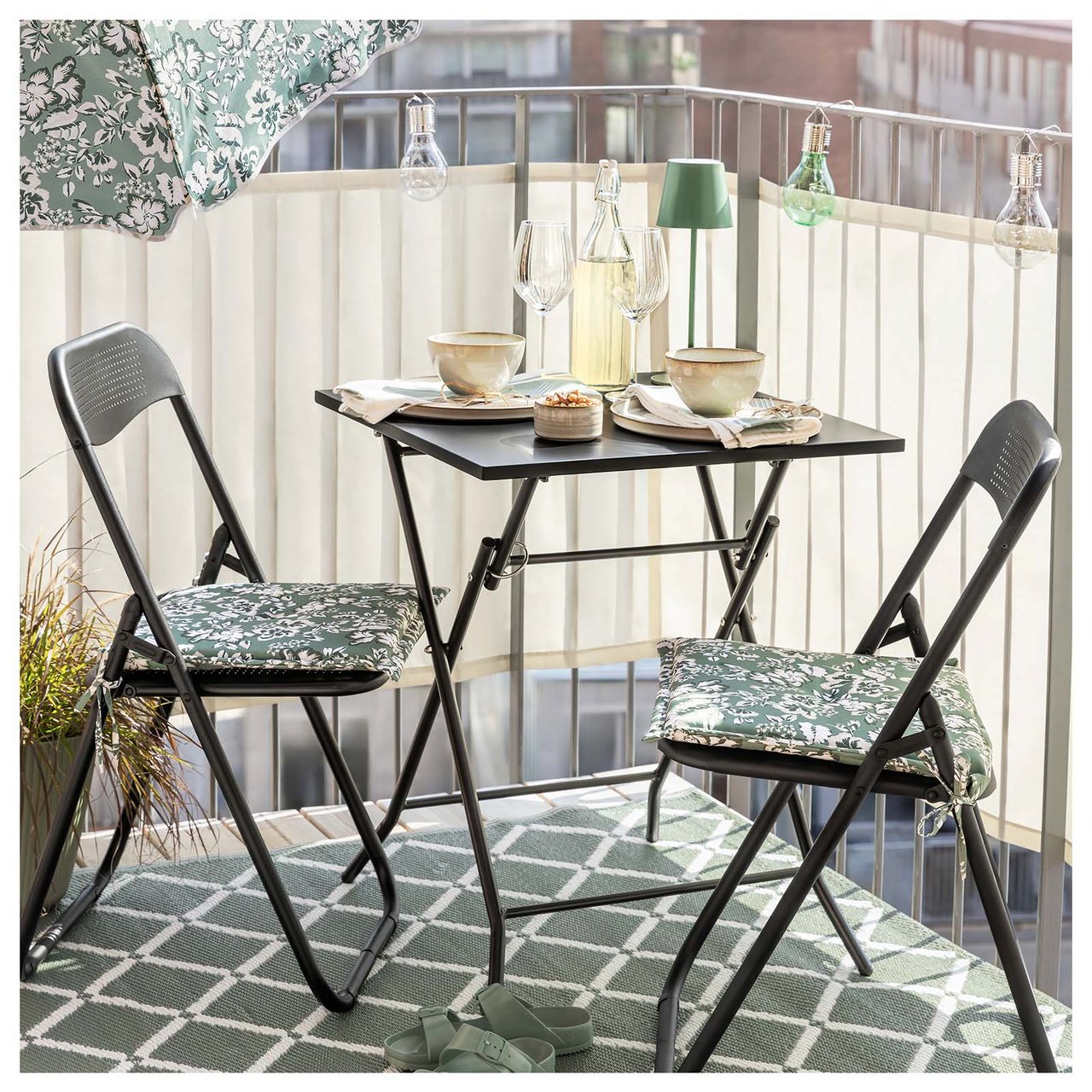 Lite kafésett med to sammenleggbare stoler og bord på en liten balkong med innsynsskjerming.