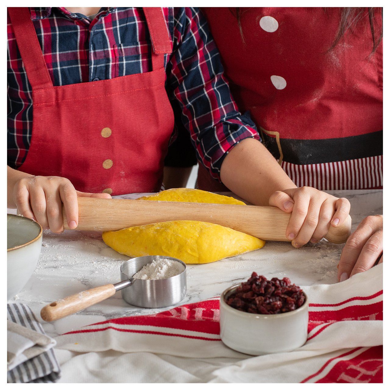 Zwei Personen rollen Safranteig auf einer Küchenarbeitsplatte aus, wo Zutaten zum Backen bereitstehen.