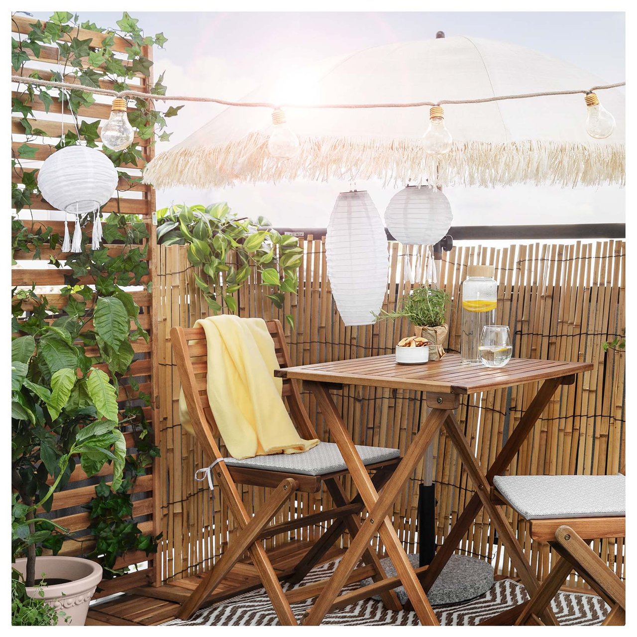 Del av balkong med ett caféset och parasoll omringas av rislampor, ljusslingor och klätterväxter.