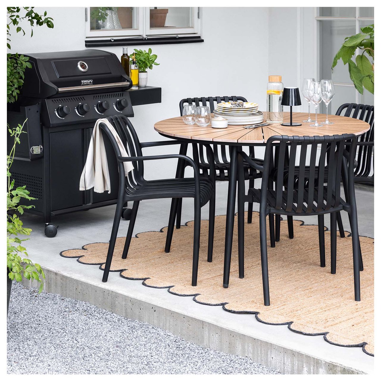 Beige juteteppe med svarte, bølgete kanter under et utebord og svarte stoler.