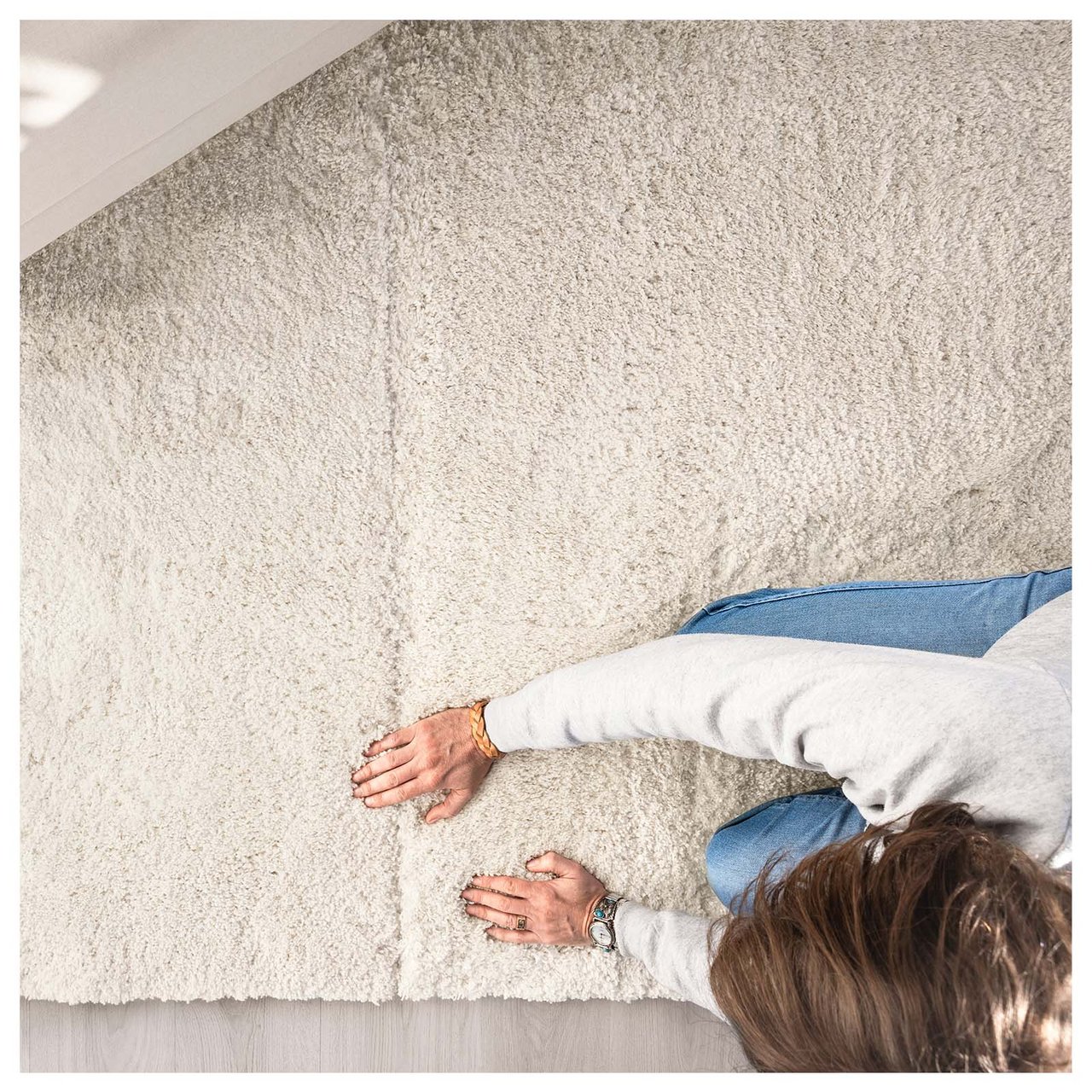 Eine dunkelhaarige Frau kniet und befühlt mit beiden Händen einen dicken naturweißen Teppich.