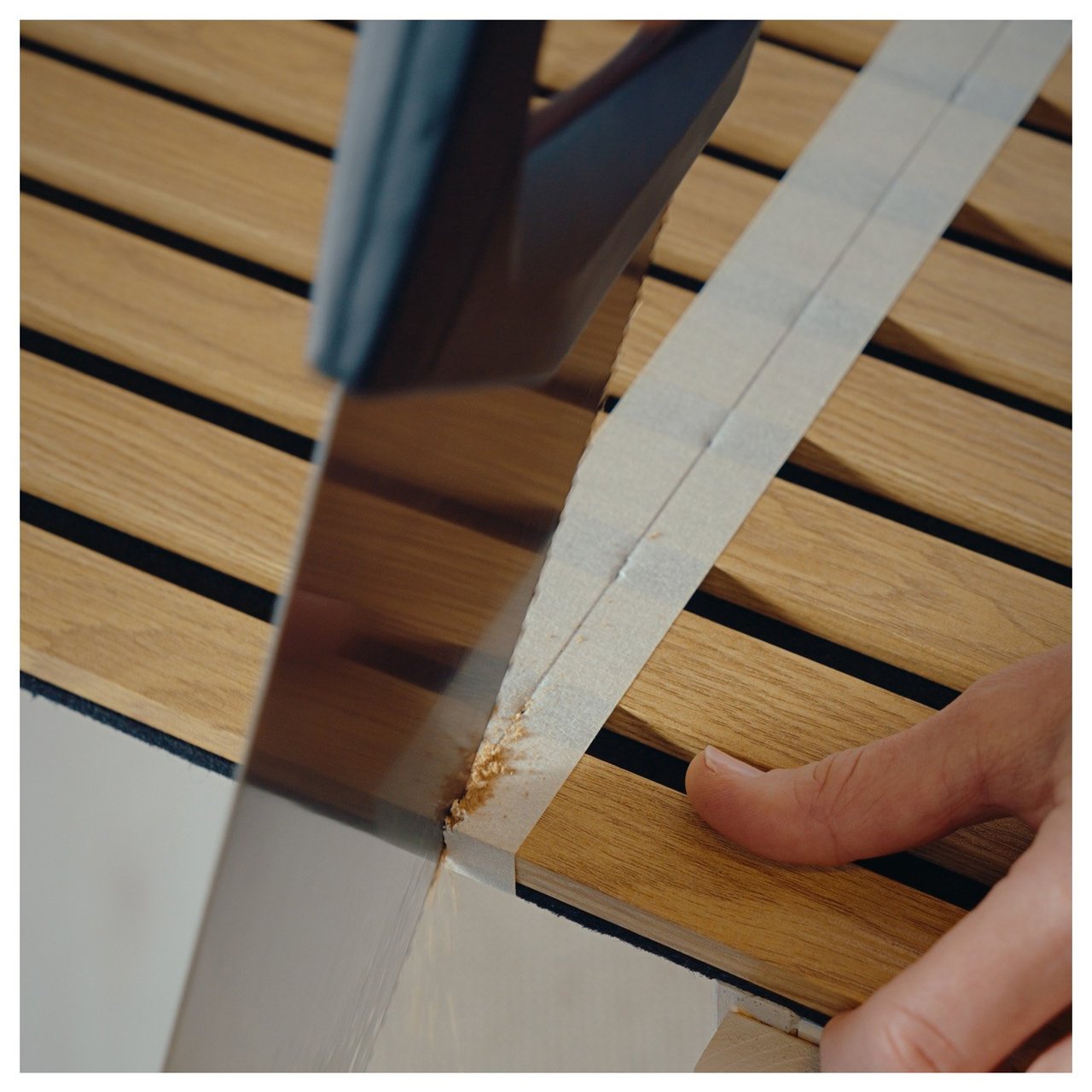 En person sågar i en akustikpanel längs en markerad tejplinje.