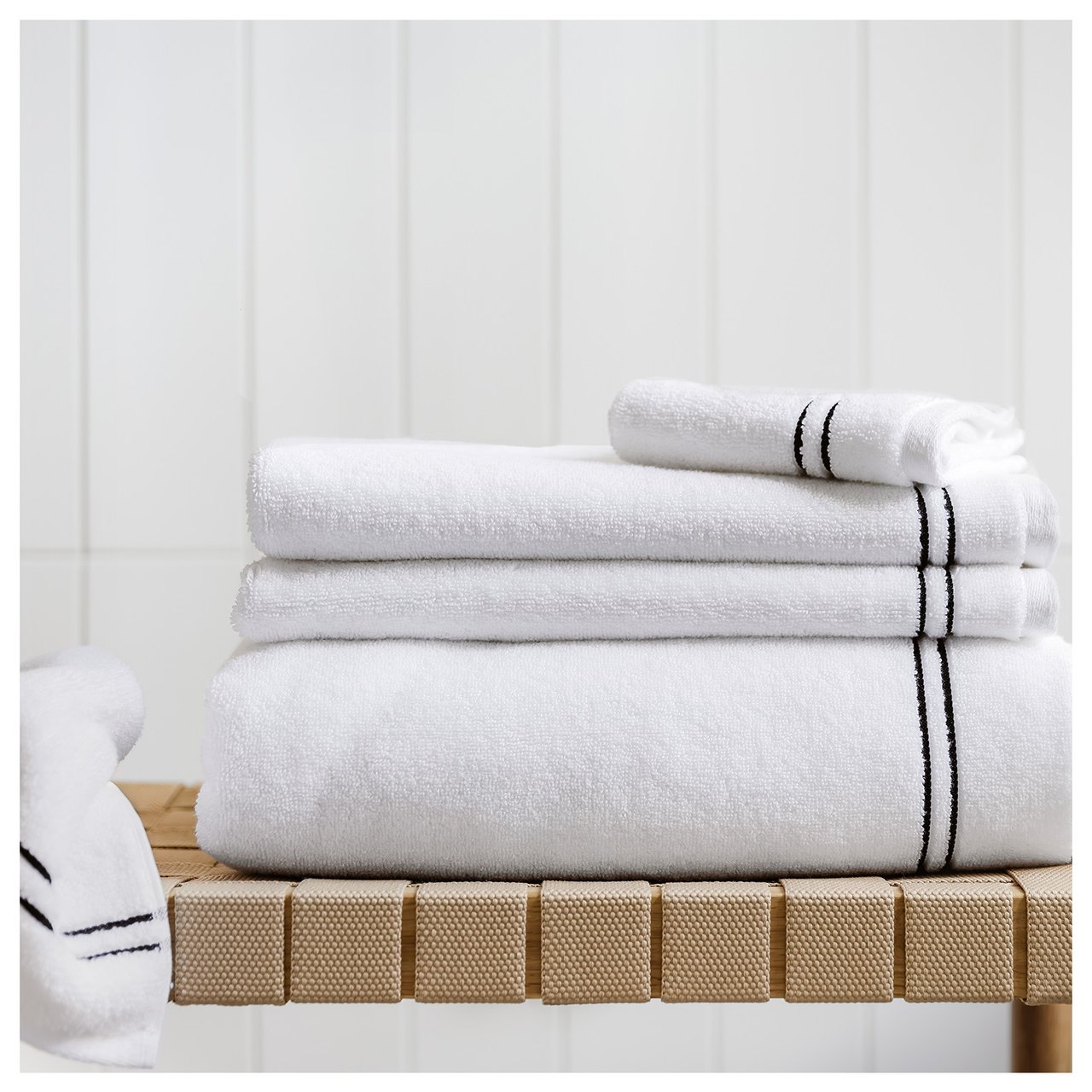 Bank mit gefalteten, weißen Handtüchern mit schwarzen Details.
