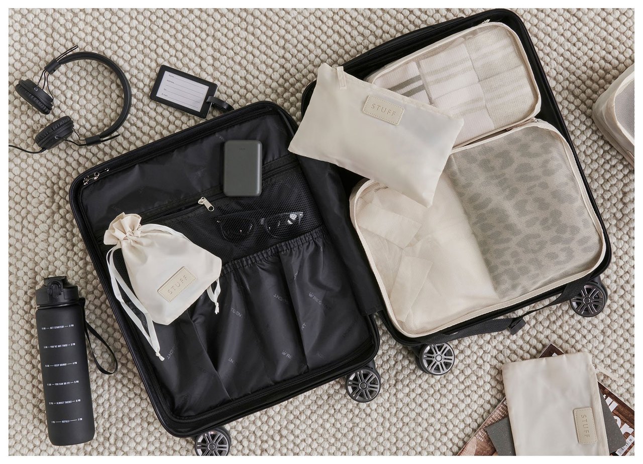 Offener Koffer mit gut organisierten Fächern und Accessoires, die auf einem Teppich für die Reise bereit liegen.