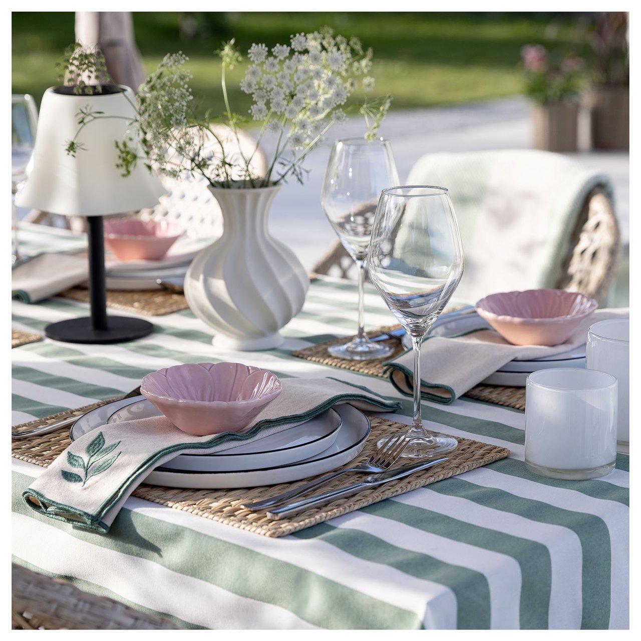 Ett dukat bord med randig duk, bordslampa och blomvas står utomhus.