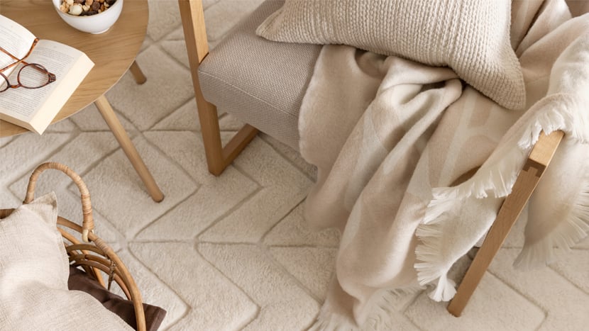 En inbjudande läshörna med fåtölj, pläd, kudde och bok placerad på en mjuk matta.