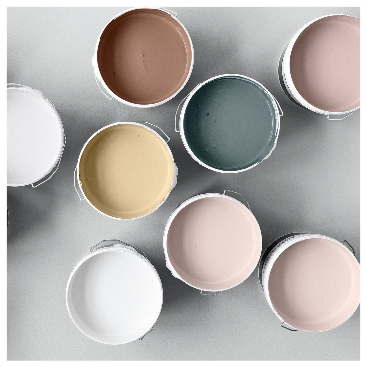 Avattuja eri värisiä maalipurkkeja asetettuna vaalealle pinnalle maalausprojektia varten.