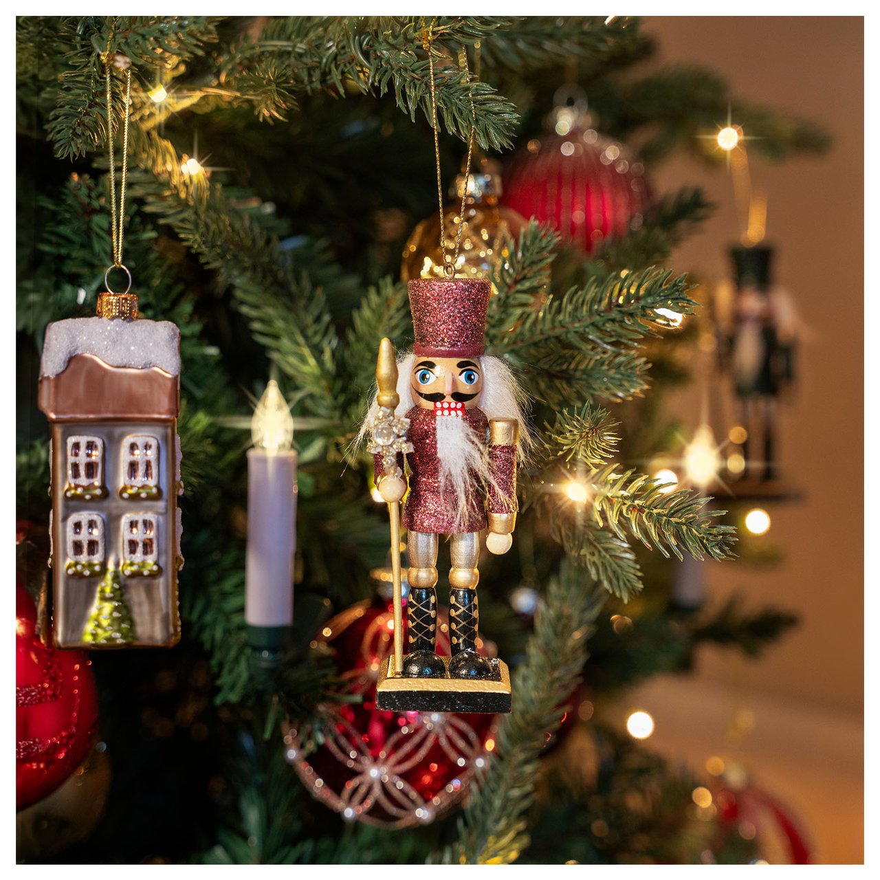 Weihnachtsbaumdekorationen in Form von Nussknackern, Häusern und Lichtern, die in einem Baum hängen.