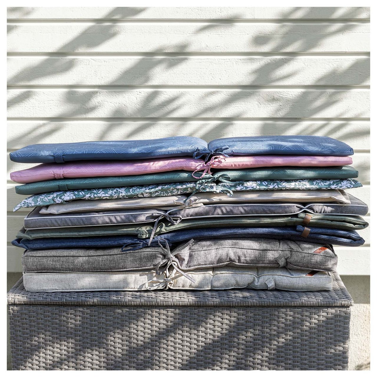 Stapel mit Rückenpolstern in verschiedenen Farben und Mustern auf einer Auflagenbox aus Kunstrattan.