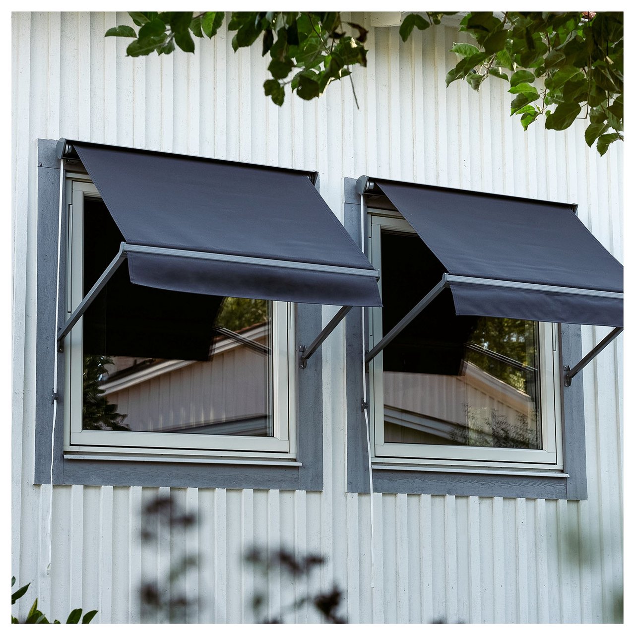 Två tättliggande fönster med mörkgrå markiser mot vit väggfasad.