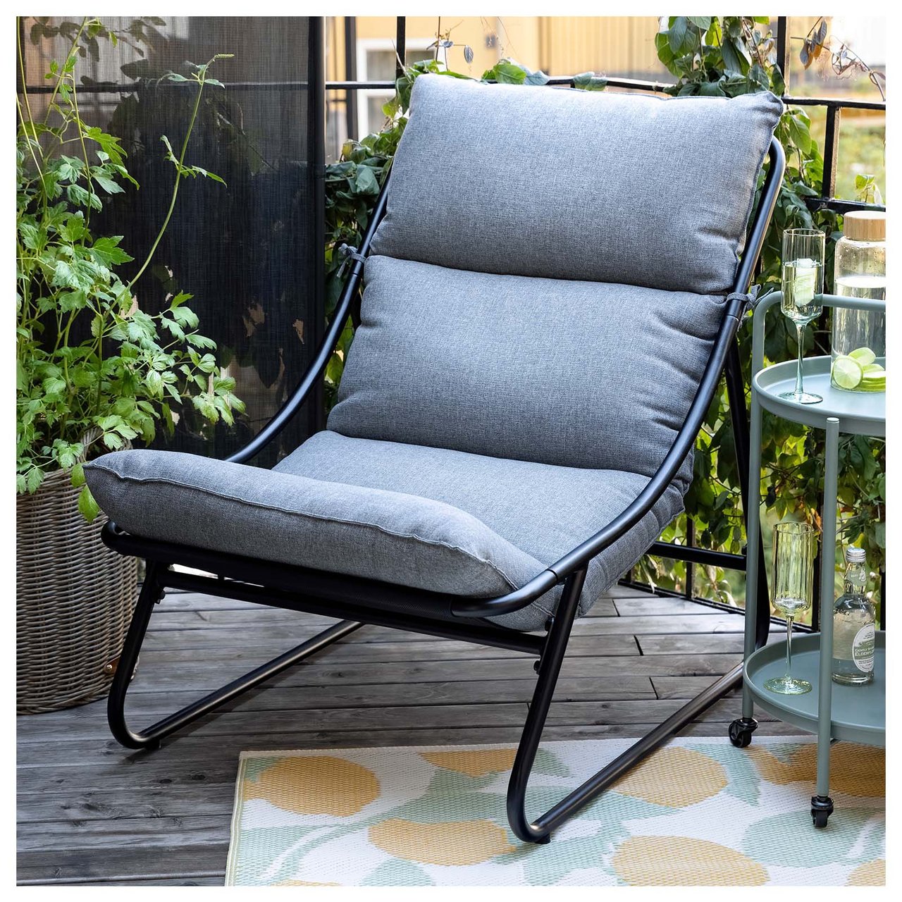 En hvilestol med grå pute står på et sitronmønstret teppe på en balkong.